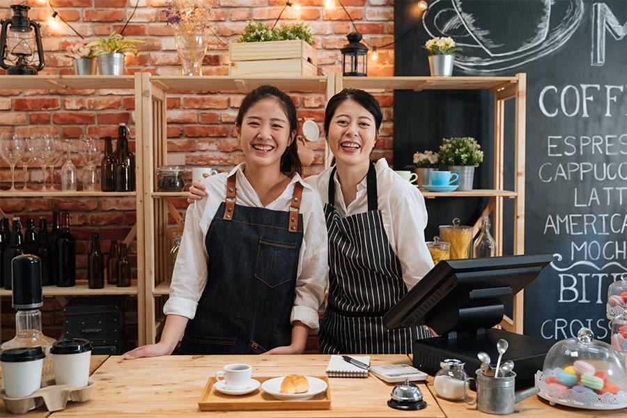 Business Insurance - Two Women Running a Cafe, Smiling and Wearing Aprons