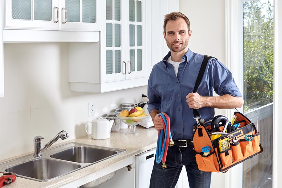Specialized Business Insurance - Contractor Holding a Tool Caddy, Pipes, and Standing by a Kitchen Sink